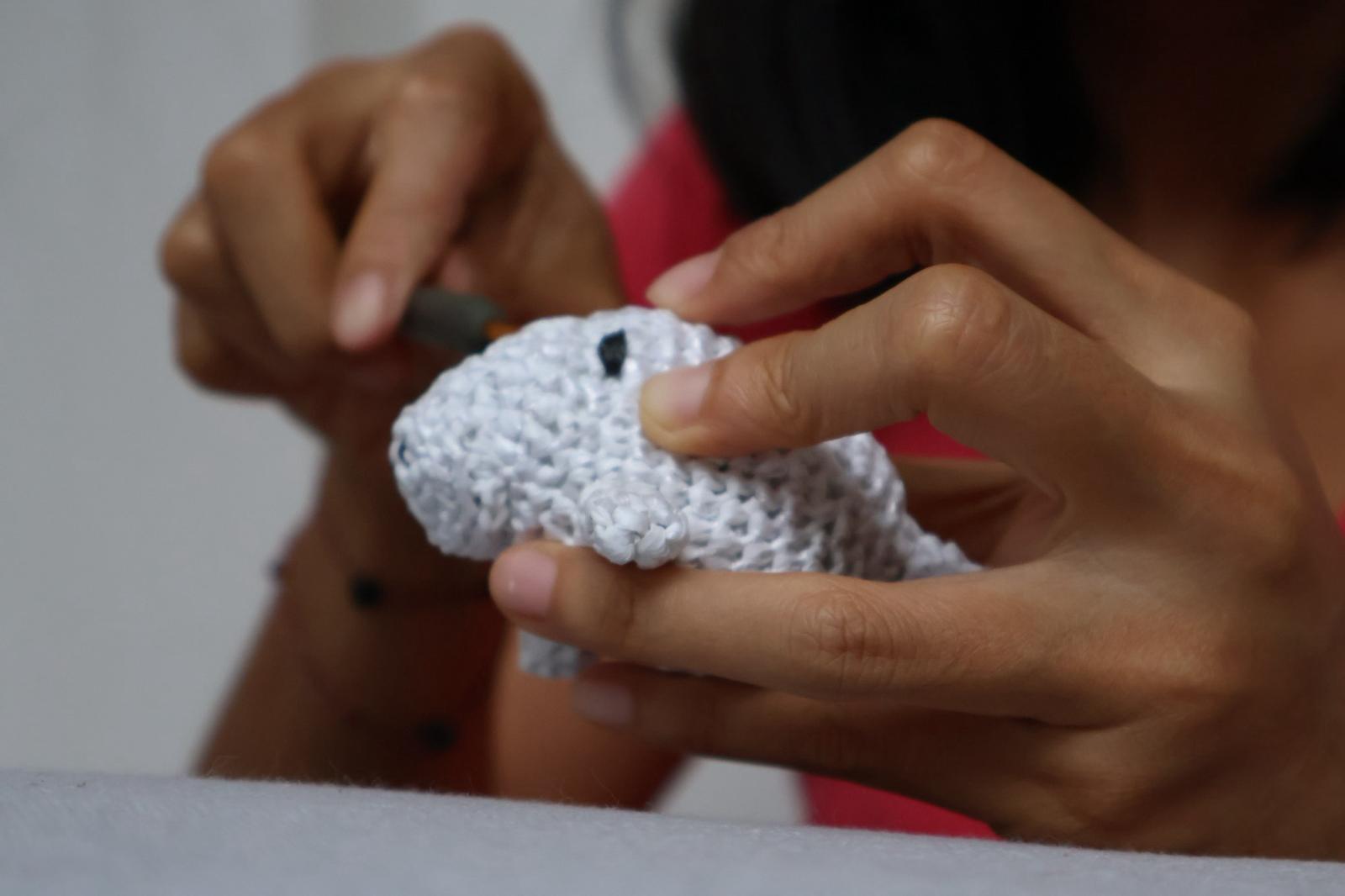 Hands crafting a white crochet animal figure from upcycled plastic waste in Indonesia